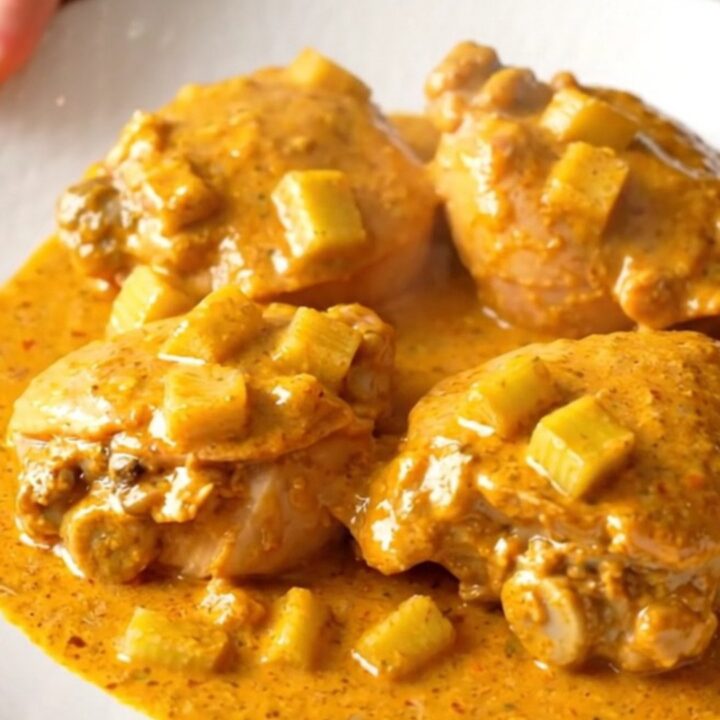 A close-up shot of creamy buffalo chicken thighs served on a white plate with visible celery pieces.