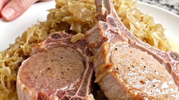 Four bone-in pork chops fanned out in a black slow cooker with sauerkraut and apple juice.