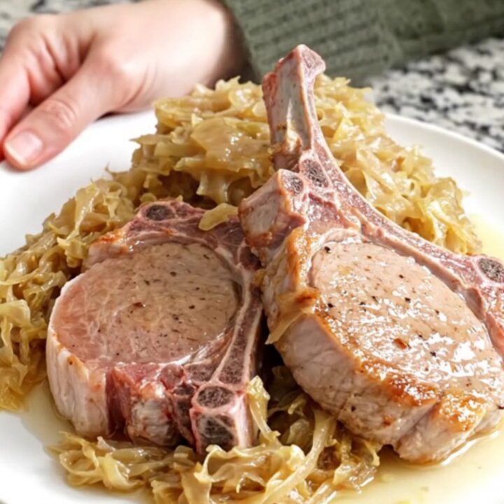 Four bone-in pork chops fanned out in a black slow cooker with sauerkraut and apple juice.