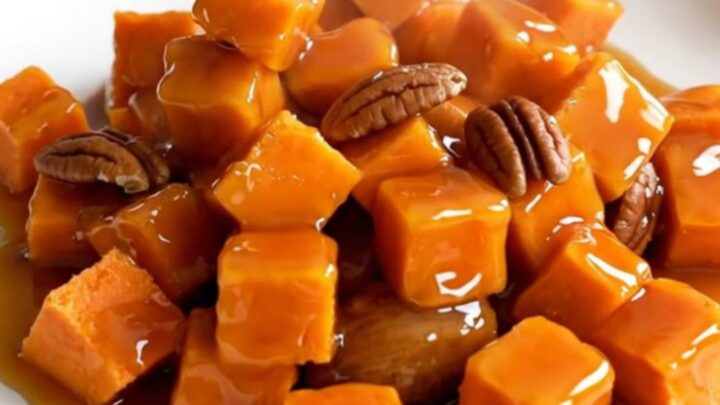 A close-up of tender, glazed sweet potato cubes mixed with toasted pecans in a black slow cooker insert.