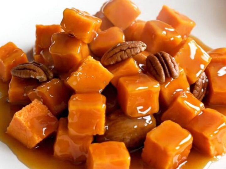 A close-up of tender, glazed sweet potato cubes mixed with toasted pecans in a black slow cooker insert.