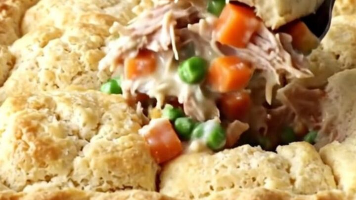 A golden-brown turkey pot pie biscuit bake in a white ceramic dish on a speckled quartz countertop.