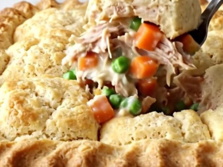 A golden-brown turkey pot pie biscuit bake in a white ceramic dish on a speckled quartz countertop.