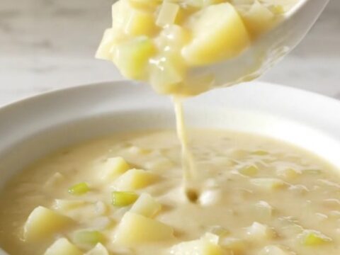 A white shallow bowl filled with creamy potato soup, garnished with herbs and steam rising from the surface.