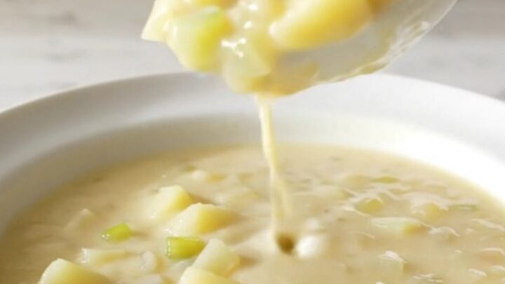 A white shallow bowl filled with creamy potato soup, garnished with herbs and steam rising from the surface.