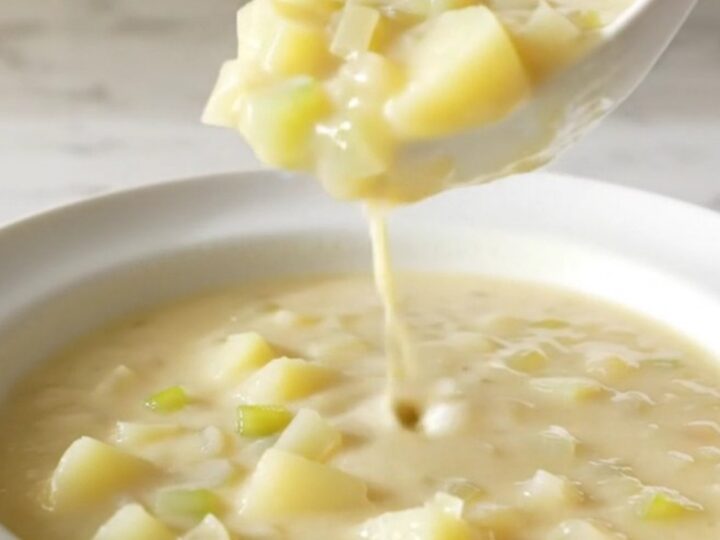 A white shallow bowl filled with creamy potato soup, garnished with herbs and steam rising from the surface.
