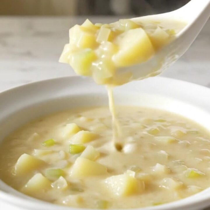 A white shallow bowl filled with creamy potato soup, garnished with herbs and steam rising from the surface.