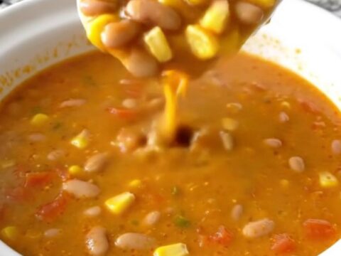 A white shallow bowl filled with creamy orange Santa Fe cheese soup, garnished with pinto beans, corn, and diced tomatoes.