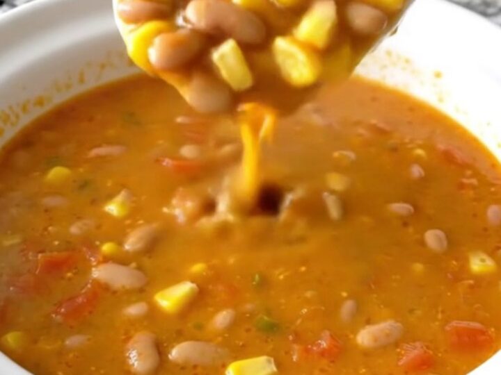 A white shallow bowl filled with creamy orange Santa Fe cheese soup, garnished with pinto beans, corn, and diced tomatoes.