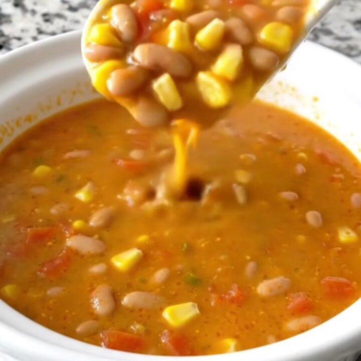 A white shallow bowl filled with creamy orange Santa Fe cheese soup, garnished with pinto beans, corn, and diced tomatoes.