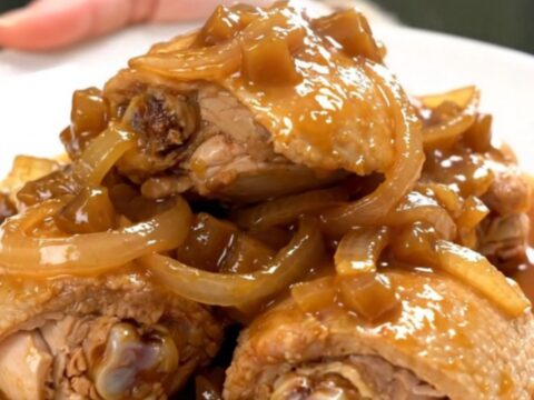 A close-up of tender chicken thighs braised in a rich, dark, and glossy apple butter sauce in a slow cooker.