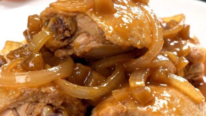 A close-up of tender chicken thighs braised in a rich, dark, and glossy apple butter sauce in a slow cooker.