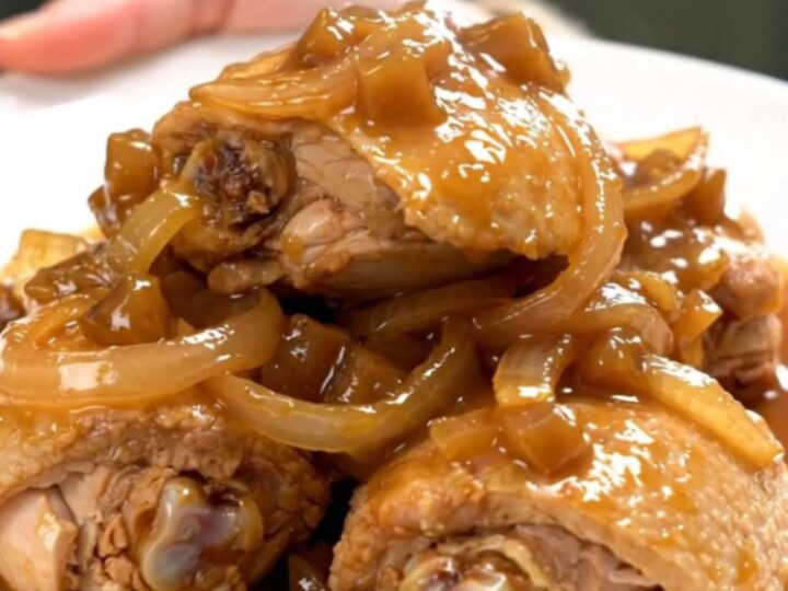 A close-up of tender chicken thighs braised in a rich, dark, and glossy apple butter sauce in a slow cooker.