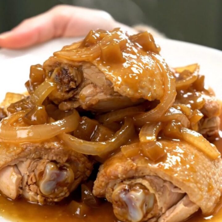 A close-up of tender chicken thighs braised in a rich, dark, and glossy apple butter sauce in a slow cooker.