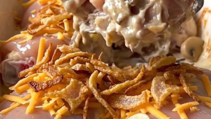 A rectangular ceramic baking dish filled with golden, baked chicken thighs covered in creamy mushroom sauce, melted cheddar