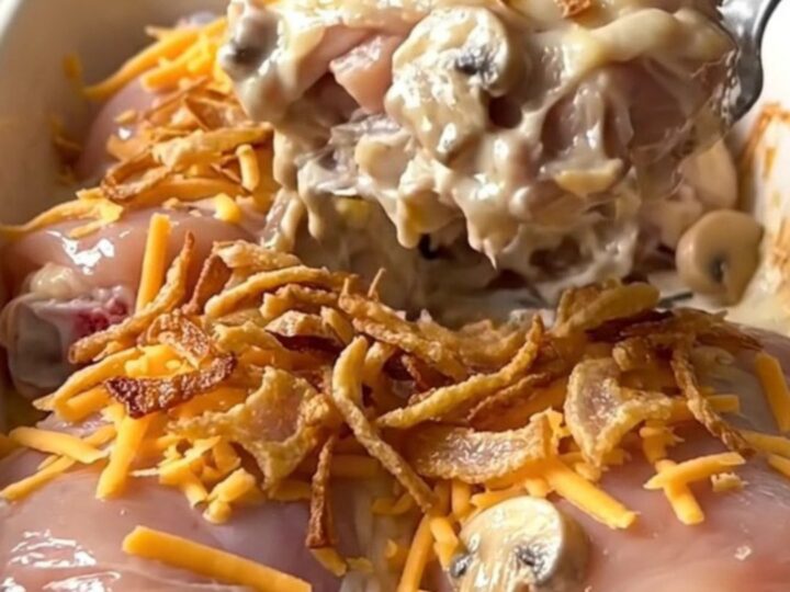 A rectangular ceramic baking dish filled with golden, baked chicken thighs covered in creamy mushroom sauce, melted cheddar
