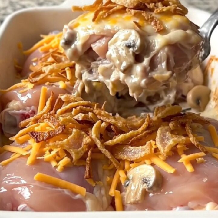 A rectangular ceramic baking dish filled with golden, baked chicken thighs covered in creamy mushroom sauce, melted cheddar