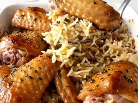 A ceramic baking dish filled with golden-brown turkey wings and fluffy herb-infused rice.