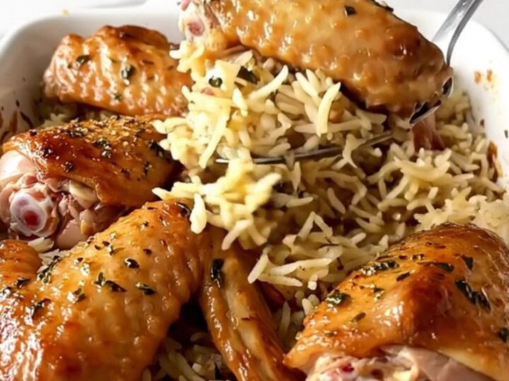 A ceramic baking dish filled with golden-brown turkey wings and fluffy herb-infused rice.