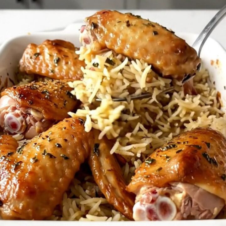 A ceramic baking dish filled with golden-brown turkey wings and fluffy herb-infused rice.