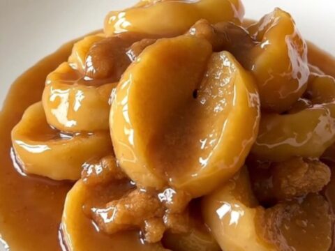 Close-up of thick, tender apple slices glazed in a rich cinnamon syrup served on a white plate.