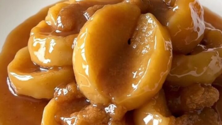 Close-up of thick, tender apple slices glazed in a rich cinnamon syrup served on a white plate.
