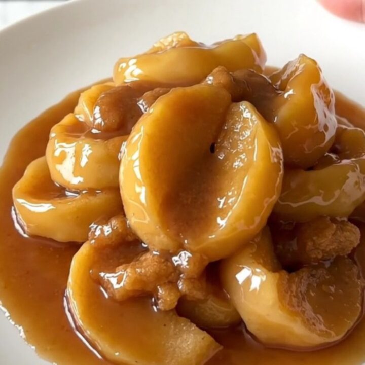 Close-up of thick, tender apple slices glazed in a rich cinnamon syrup served on a white plate.