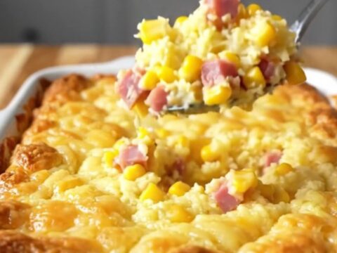 A top-down view of a rectangular baking dish filled with a golden, baked ham and cheddar corn pudding casserole.