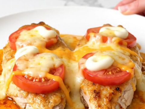 A top-down view of a slow cooker filled with chicken breasts topped with sliced tomatoes and melted cheese.