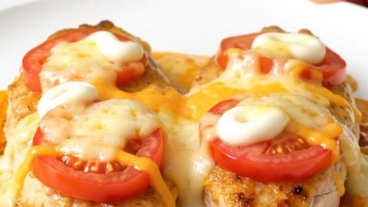 A top-down view of a slow cooker filled with chicken breasts topped with sliced tomatoes and melted cheese.