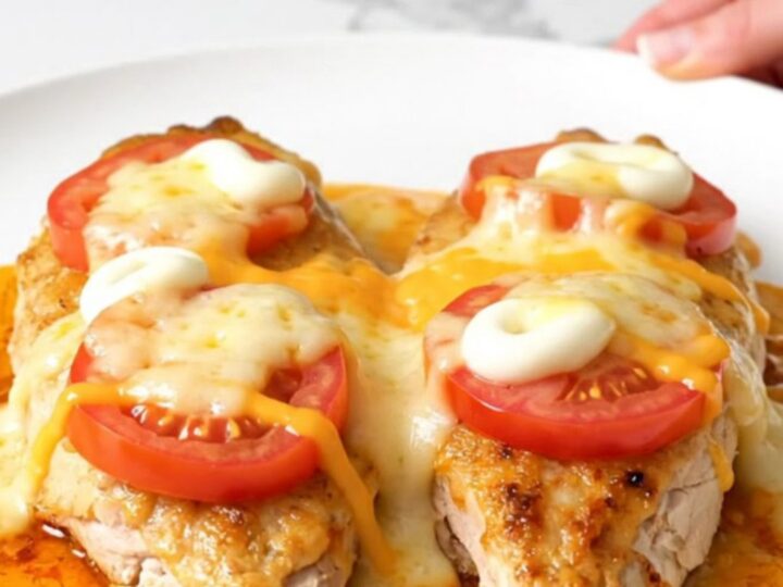 A top-down view of a slow cooker filled with chicken breasts topped with sliced tomatoes and melted cheese.