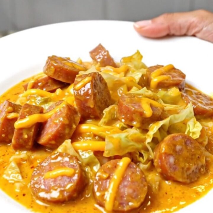 A top-down view of a slow cooker filled with sliced smoked sausage, chopped green cabbage, and a creamy cheddar sauce.