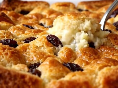 A golden-brown raisin bread pudding in a white ceramic dish, freshly baked and ready to serve.