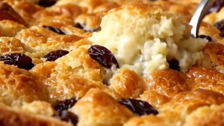 A golden-brown raisin bread pudding in a white ceramic dish, freshly baked and ready to serve.