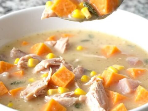 A steaming bowl of creamy turkey and sweet potato chowder with visible corn and sage.