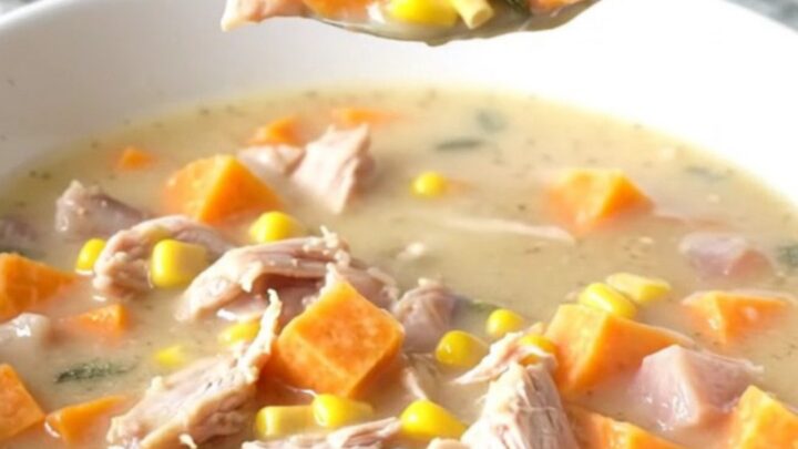 A steaming bowl of creamy turkey and sweet potato chowder with visible corn and sage.