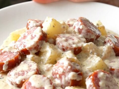 A close-up of a serving of creamy slow cooker Alfredo sausage and potatoes on a white plate.