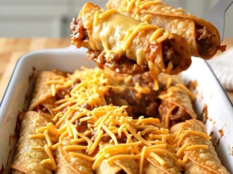 A large rectangular baker filled with golden-brown beef taquitos topped with hearty beef chili and melted cheddar cheese.