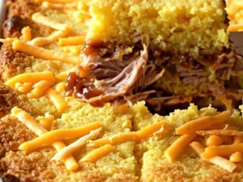 A golden, bubbling BBQ pulled pork cornbread casserole in a white ceramic baking dish.