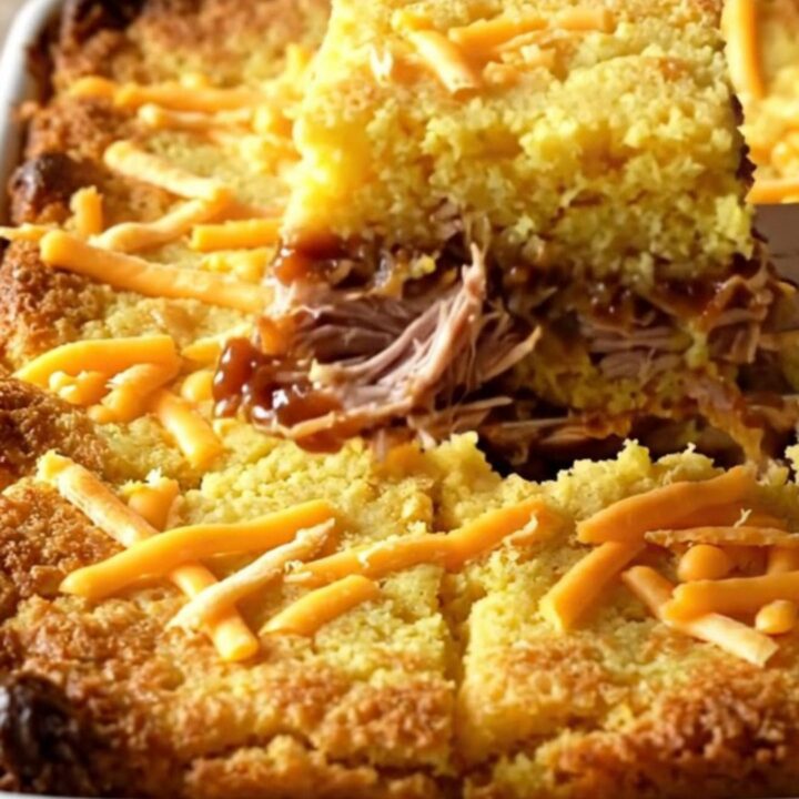 A golden, bubbling BBQ pulled pork cornbread casserole in a white ceramic baking dish.