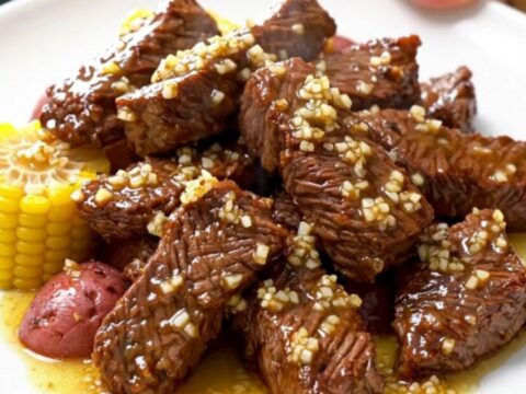 A close-up of tender beef tips, corn cob rounds, and halved baby red potatoes in a savory Cajun garlic butter sauce.