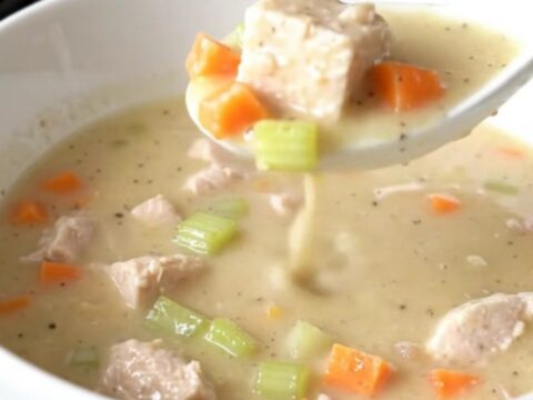 A shallow white bowl filled with creamy chicken velvet soup featuring visible chicken cubes and carrots.