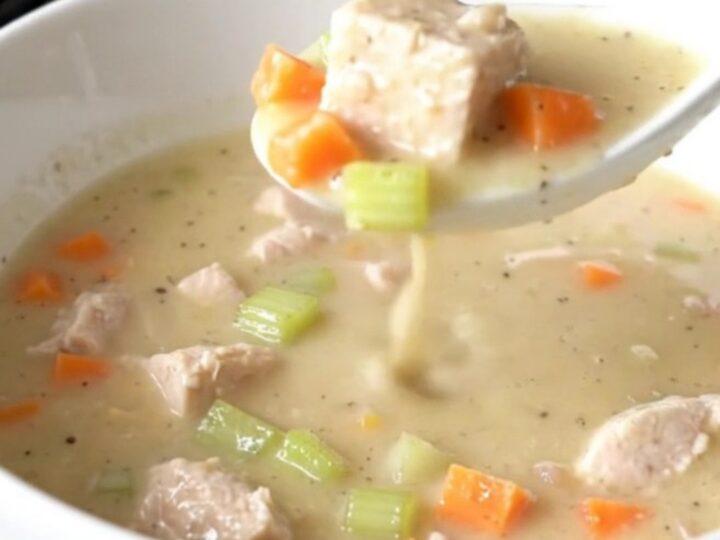 A shallow white bowl filled with creamy chicken velvet soup featuring visible chicken cubes and carrots.