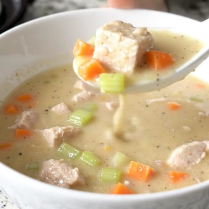 A shallow white bowl filled with creamy chicken velvet soup featuring visible chicken cubes and carrots.