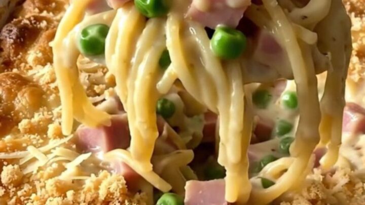 A top-down view of a creamy ham and pea tetrazzini casserole in a rectangular white baker on a granite counter.