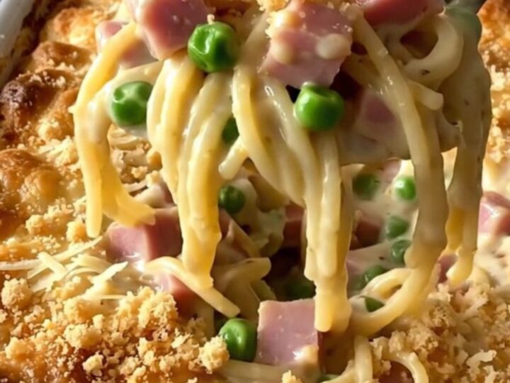 A top-down view of a creamy ham and pea tetrazzini casserole in a rectangular white baker on a granite counter.