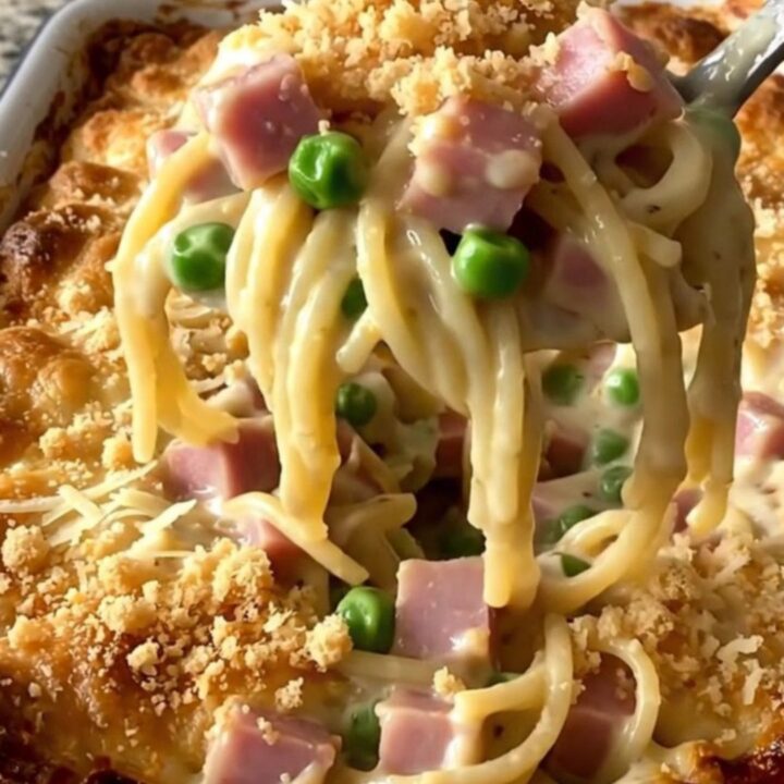 A top-down view of a creamy ham and pea tetrazzini casserole in a rectangular white baker on a granite counter.