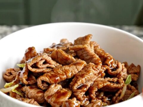 A shallow white bowl filled with braised pork, shredded cabbage, and carrots in a savory soy-ginger sauce.