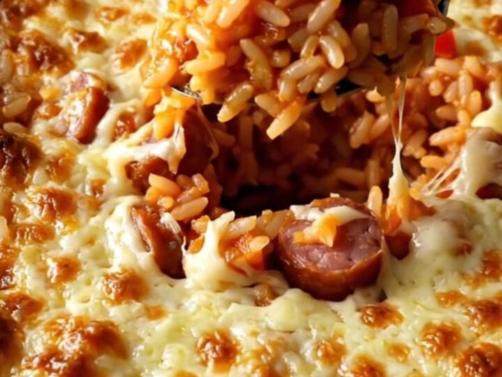 A top-down view of a ceramic baking dish filled with rice, smoked sausage coins, and diced bell peppers.