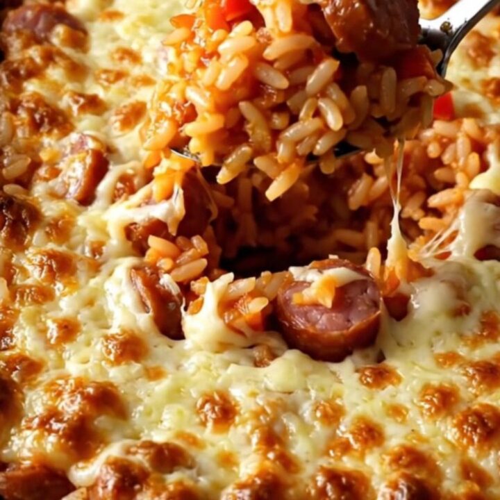 A top-down view of a ceramic baking dish filled with rice, smoked sausage coins, and diced bell peppers.